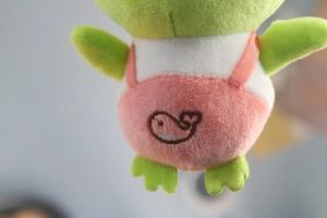 Detailed close-up of a green plush frog wearing pink overalls with whale embroidery