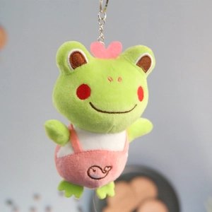Close-up of cute green frog plush keychain with heart decor and pink overall pants