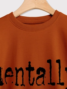 Gros plan du col côtelé et de l'impression de lettres noires sur ce sweat orange-marron