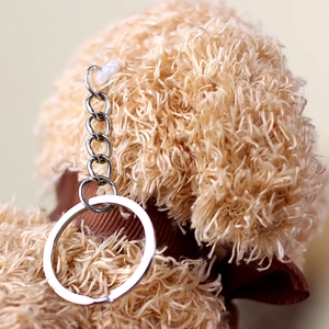 Detailed macro view of the silver metal keychain attachment on a curly teddy dog plush toy