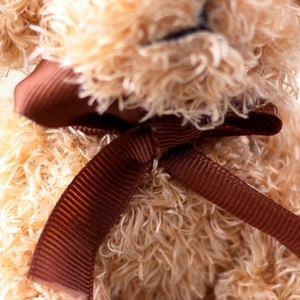Detailed close-up of a plush teddy dog featuring a dark brown ribbed ribbon bowtie