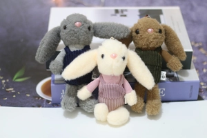 Detailed view of plush rabbit charms wearing corduroy overalls on white books
