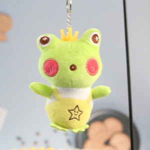 Cute green frog plush keychain with yellow crown and star dungarees on blue background