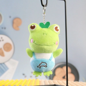 Cute long-legged frog plush keychain with blue overalls hanging on a metal stand