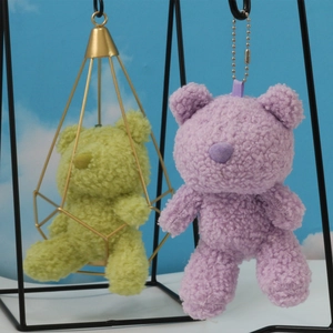 Detail of plush teddy bear keychains in purple and green with curly fleece texture