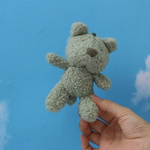Sage green teddy bear plush keychain in hand showing soft curly fur texture and size
