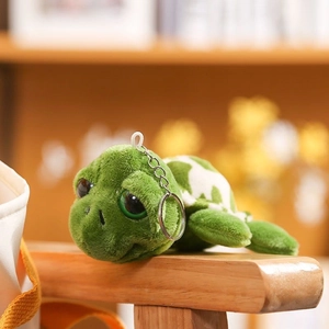 Cute green plush turtle keychain with large eyes on a wooden stand for backpack decor