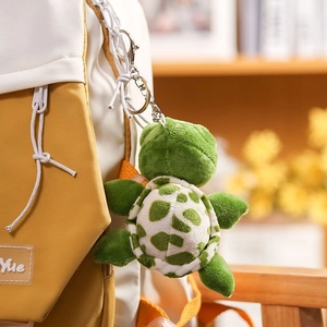 Cute green plush turtle keychain with spotted shell hanging on a canvas backpack
