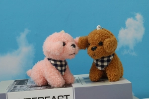 Close-up of pink and brown plush puppy keychains with plaid scarves on a display box