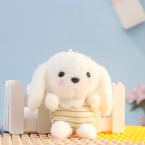 Detailopname van schattige witte pluche puppy sleutelhanger met geel en paars gestreept vest