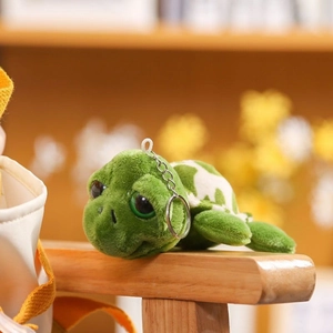 Cute green plush turtle keychain with white shell patterns on a wooden railing