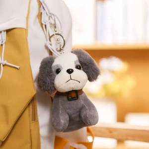 Cute gray puppy plush keychain with leather collar hanging on a canvas bag strap