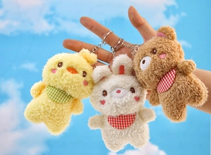 Three plush animal keychains with checkered scarves held against a clear blue sky