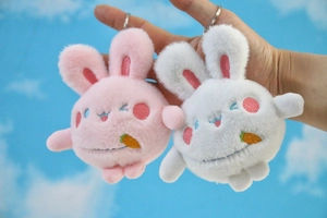 Close-up of pink and white plush bunny keychains with embroidery held in hand