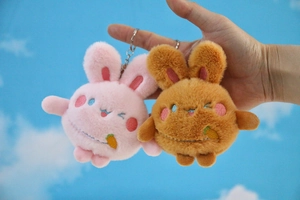 Close-up of pink and brown plush bunny keychains with embroidery on blue sky backdrop