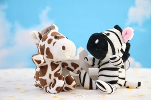 Plush giraffe and zebra keychains shown in a playful outdoor-themed miniature garden