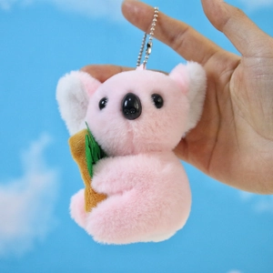 Portachiavi koala in peluche rosa con foglia verde tenuto su uno sfondo di cielo blu