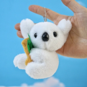 Dettaglio di un portachiavi a forma di koala in peluche bianco con bambù marrone e foglie