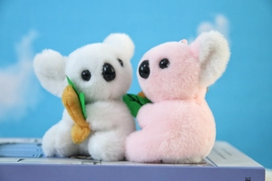 Portachiavi koala in peluche rosa e bianco seduti su un libro decorativo viola soft