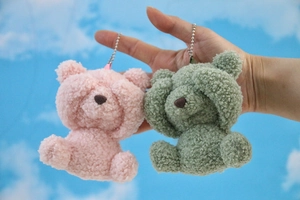 Detail view of pink and green plush bear pendants with metallic chains and teddy fleece texture