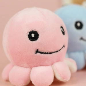 Close-up of a pink plush octopus keychain with delicate black embroidered facial expressions