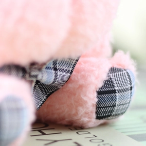 Close-up of pink plush fur texture with a classic plaid ribbon bow and fabric foot detail