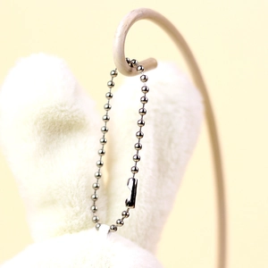 Detailed macro view of a silver metal bead chain connector on a white plush toy