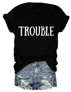 Dettaglio della stampa TROUBLE su t-shirt nera e pantaloncini di jeans blu con strappi