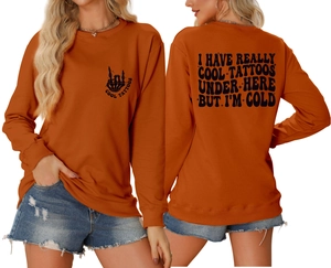 Close-up of orange crewneck sweatshirt featuring black tattoo slogan and skull graphics