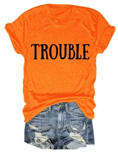 Dettaglio della maglietta arancione con scritta TROUBLE e pantaloncini di jeans strappati