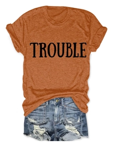 Dettaglio della t-shirt in cotone arancione con stampa TROUBLE e shorts in denim