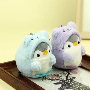 Dettaglio di portachiavi in peluche a forma di pinguino blu e viola su un vassoio di legno