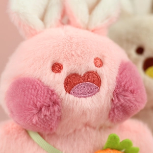 Dettaglio ravvicinato di coniglio rosa di peluche con occhi ricamati e borsa carota