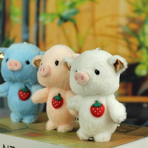 Detailed view of pink, white and blue plush pig keychains with cute strawberry badges