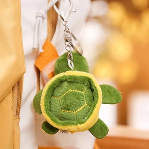 Detailed view of plush turtle keychain with green shell and yellow stitching on a bag