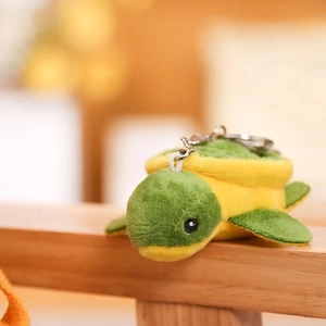 Close-up of green and yellow plush turtle keychain with a sturdy metal ring on wood