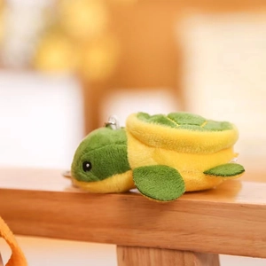 Cute green plush turtle keychain with yellow shell details and soft texture on wood