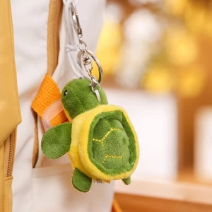 Detail of cute turtle plush charm with yellow stitching hanging on a white backpack