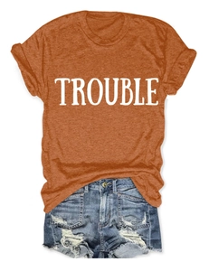 Dettaglio della maglietta in cotone arancione con scritta TROUBLE e shorts in denim