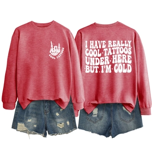 Flat lay of red crewneck sweatshirt with 'I HAVE REALLY COOL TATTOOS' text and ripped denim