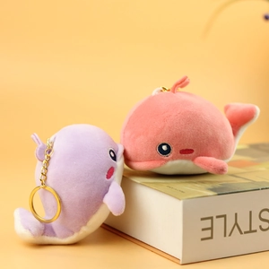 Cute plush whale keychain pendants in purple and pink displayed on a white book decor