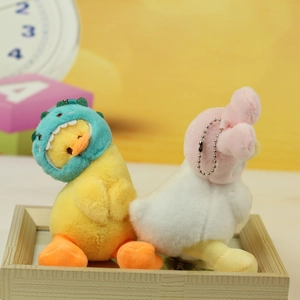 Close-up of cute plush duck pendants in dinosaur and bunny hats on a wooden tray