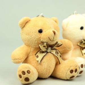 Close-up of soft plush teddy bear charms in brown and beige with paw-print ribbons