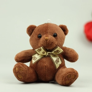 Close-up of brown plush teddy bear keychain featuring a golden satin bow with paw prints