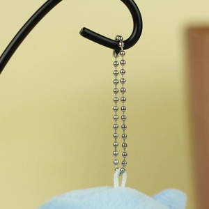 Detail of silver bead chain and white fabric loop on a light blue plush keychain charm