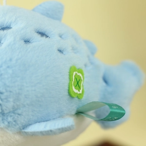 Close-up of soft light blue plush fabric with green clover embroidery and satin brand ribbon