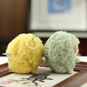 Close-up of yellow and green plush sheep keychains in a wooden frame with floral card