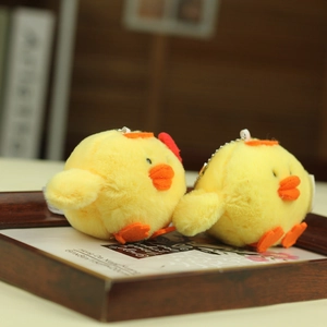 Close-up of two soft yellow plush chick keychains with orange beaks on a wooden tray