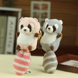 Detail of plush raccoon keychains with striped tails in pink and grey on a desk