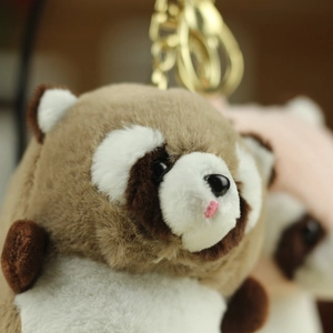 Close-up of cute raccoon plush keychain with soft fur and golden lobster clasp